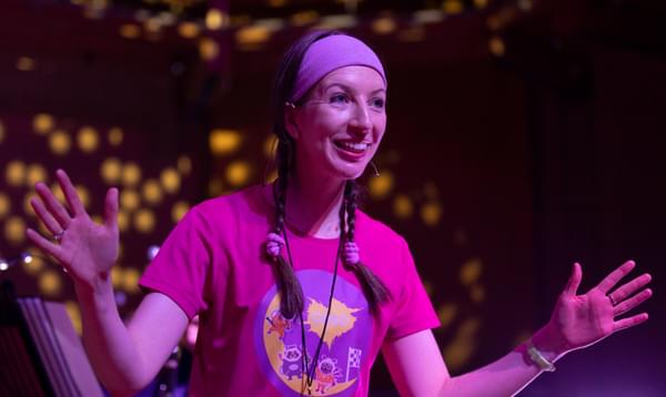 Photograph of Bryony Morrison presenting a Key Stage 1 concert with sparkling lights behind her