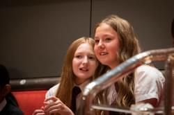 Photograph of two girls in school uniform watching a performance