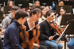 Photograph of two young violinists looking at their music and talking in a rehearsal.