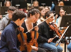 Photograph of two young violinists looking at their music and talking in a rehearsal.