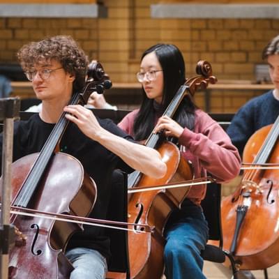 Photo of three young cellists playing in a rehearsal.