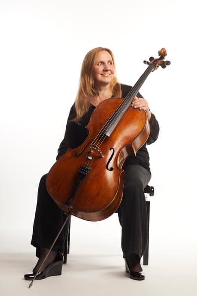 Profile photograph of Helen Edgar sitting with her cello and smiling
