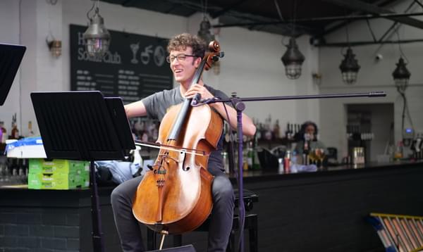 Photograph of Arthur Boutillier playing the cello and laughing at Hockley Social Club