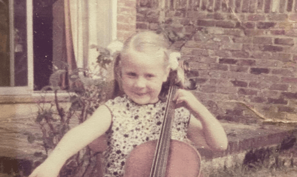 Helen Edgar is pictured at as a child playing the cello. Helen is sat outside. The image is slightly muted in colour due to age.