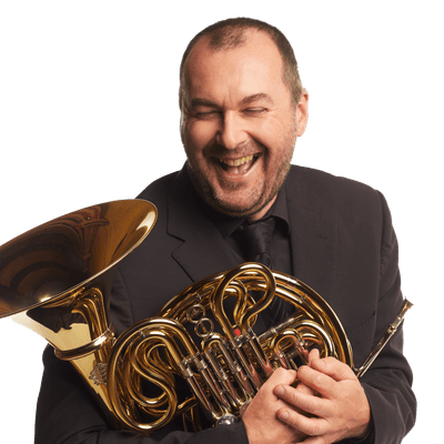 Headshot of french horn player Jeremy Bushell. Jeremy is laughing and is holding his french horn to his chest.