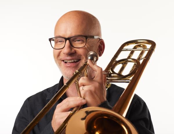 Headshot of trombonist Anthony Howe. He is smiling and holding his trombone.
