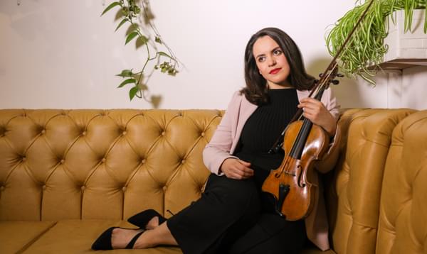 Photograph of Colette Overdijk with her violin sitting on a sofa