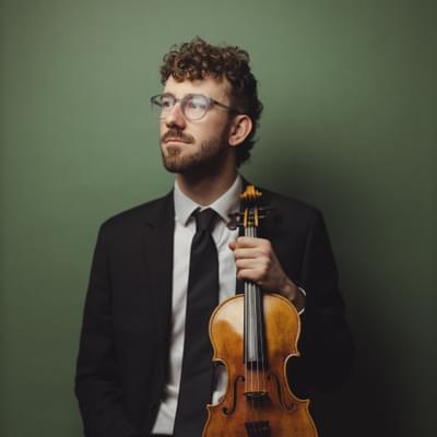 Headshot of Violinist Jack Greed. Jack is holding his violin.
