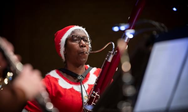 Margaret is playing the bassoon, dressed in a red Christmas outfit and hat.