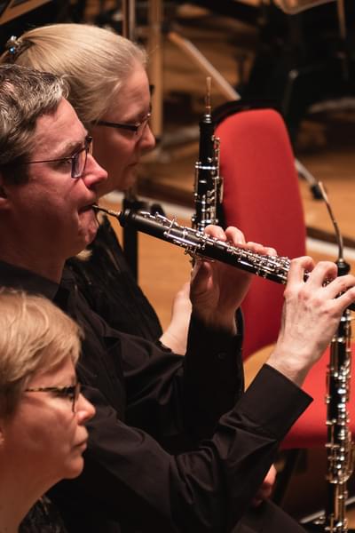 Emmer Byrne is playing the oboe during a concert. He is surrounded by other players in the orchestra