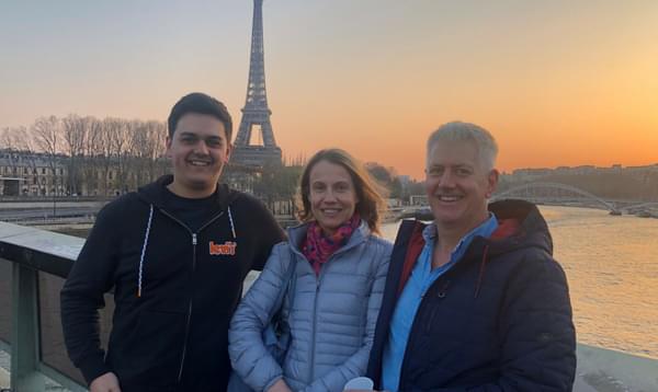 Oliver Janes, Jo Patton, and Mark Goodchild are stood by the River Seine with the Eifel Tower in the background. The sun is setting in the background.