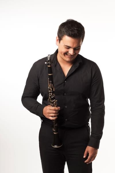 Headshot of clarinetist Oliver Janes. Oliver is looking down and smiling, holding his clarinet in his right hand.