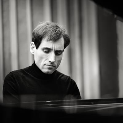 Black and white photograph of Boris Giltburg playing the piano whilst wearing a black turtleneck.