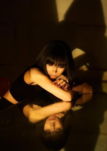 Photograph of Alice Sara Ott leaning against the top of a grand piano