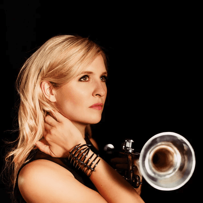 Headshot of trumpeter Alison Balsom. She is looking to the side and holding her trumpet towards the camera.