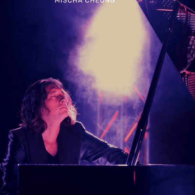 Photograph of pianist Mischa Cheung. Mischa is playing the piano on stage, with a bright light behind him.