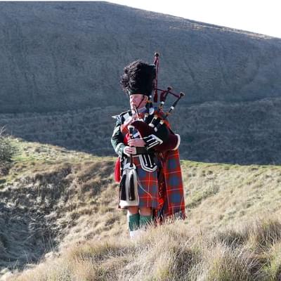 Photo of Robert Jordan playing the bagpipes in a field
