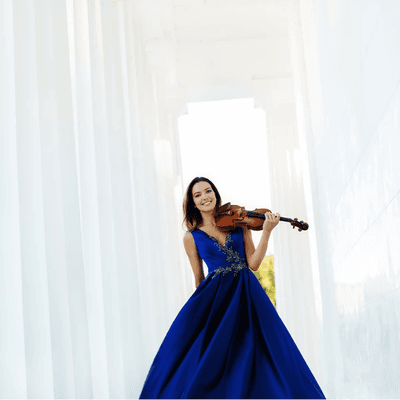 Photography of violist Sarah McElravy. She is stood between white pillars, holding her viola.