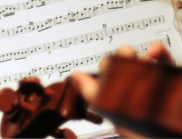 Photo of sheet music, with a close up of someone playing the violin in the foreground of the image.