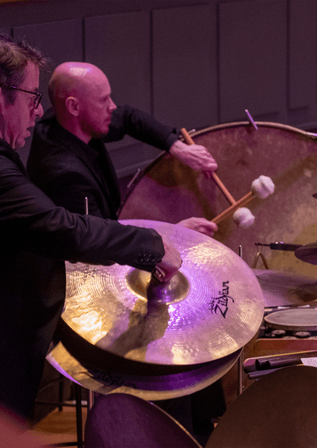 Photograph of two percussionists playing the cymbals and bass drum at Symphony Hall.