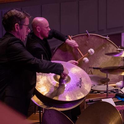 Photograph of two percussionists playing the cymbals and bass drum at Symphony Hall.
