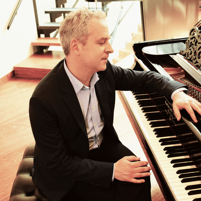 Photograph of Jeremy Denk sitting at a piano.