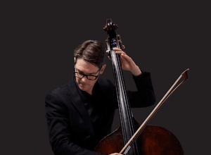 Photograph of Jeremy Watt playing the double bass on a black background.