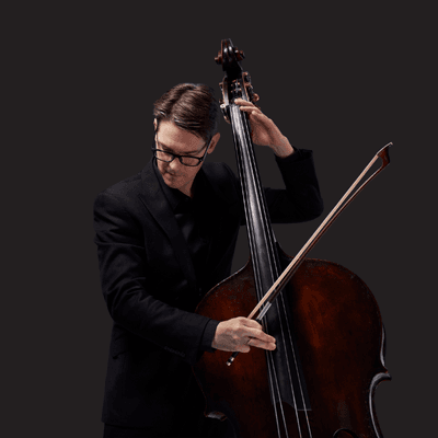 Photograph of Jeremy Watt playing the double bass on a black background.