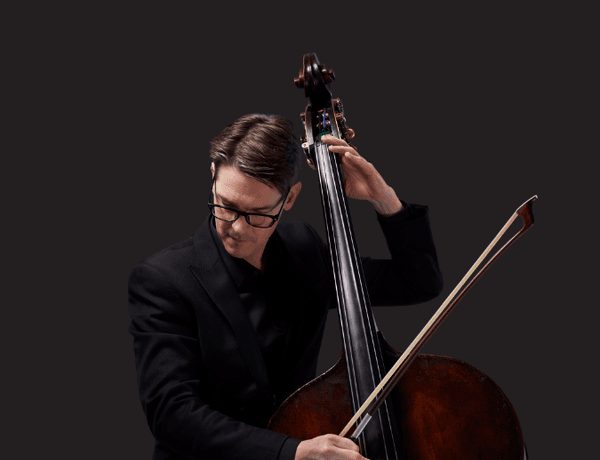 Photograph of Jeremy Watt playing the double bass on a black background.