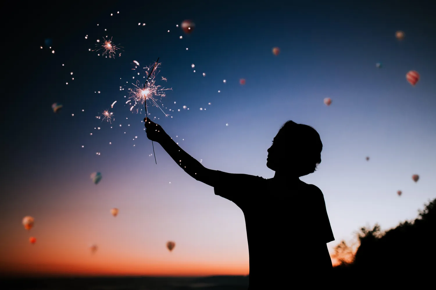 Child holding sparkler in lit sky