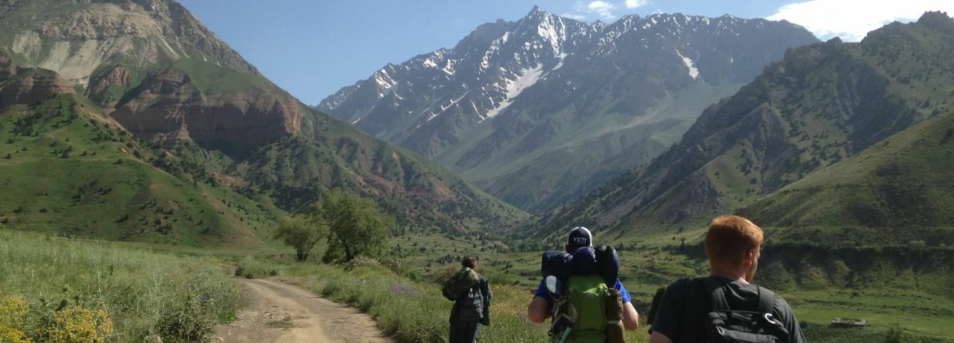 Three participants hike down a road surrounded by tall mountains.