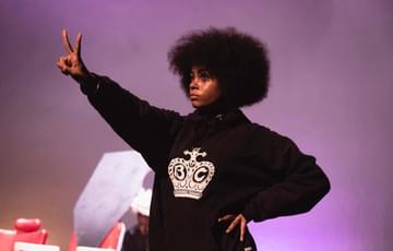 A young person with an afro holds up a peace sign