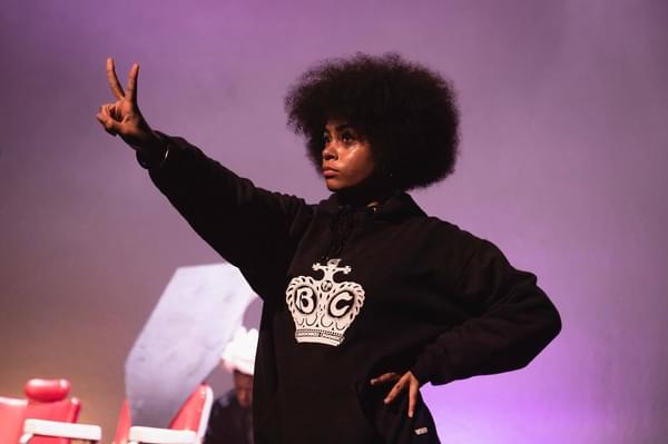 A young person with an afro holds up a peace sign