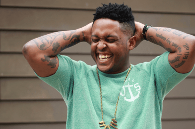 Danez Smith with their arms lifted, laughing.