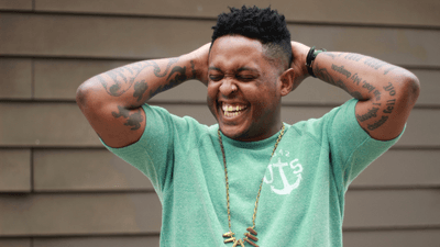 Danez Smith with their arms lifted, laughing.