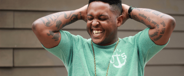 Danez Smith with their arms lifted, laughing.