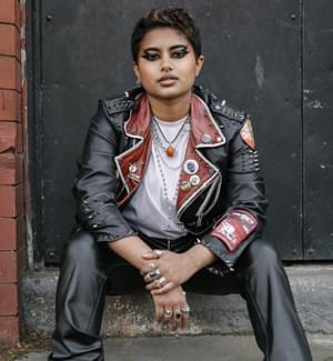 person sitting on a step posing at the camera wearing a leather jacket