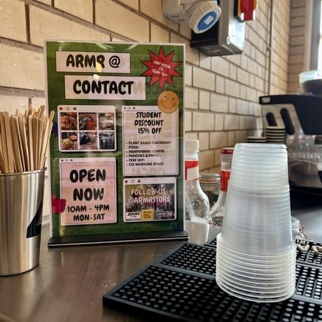 Green leaflet of ARMR at the centre. On the right is a stack of clear plastic cups and on the left is a cup of stirrers.