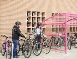 Two people holding their bikes next to the pink bike shed.