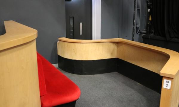 View of one of the Space 1 wheelchair accessible Box seats from behind. The seats are red and there is a wooden barrier in front.
