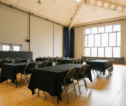 Large rehearsal room with several tables covered with black table cloths and chairs around them