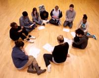 A group of young people sit on the floor in a circle during a workshop