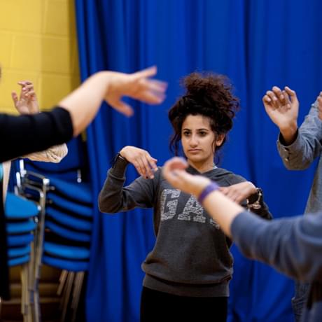 A group of young people perform in a circle, hands waving, in a rehearsal room