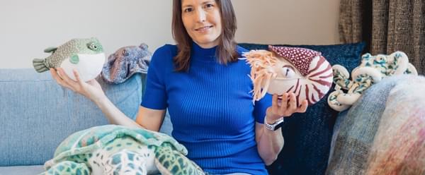 Dr Helen Czerski seated on a sofa holding various stuffed toy ocean creatures.