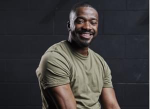 A picture of the chairman of our Board, Junior. A black male in a green t-shirt smiling and looking relaxed