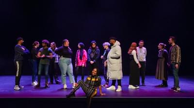 Keisha Thompson sat on the edge of the stage with members of the Contact staff team chatting behind her