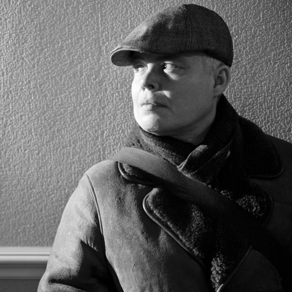 A black and white image of a woman in wearing a coat, scarf and flat cap