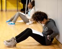 A young person sits in a rehearsal room reading a script on their knees