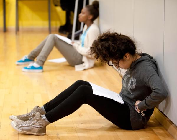 A young person sits in a rehearsal room reading a script on their knees