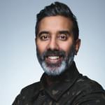 A man in his 50's of Sri Lankan heritage with a beard smiling and wearing a camouflage patterned jacket